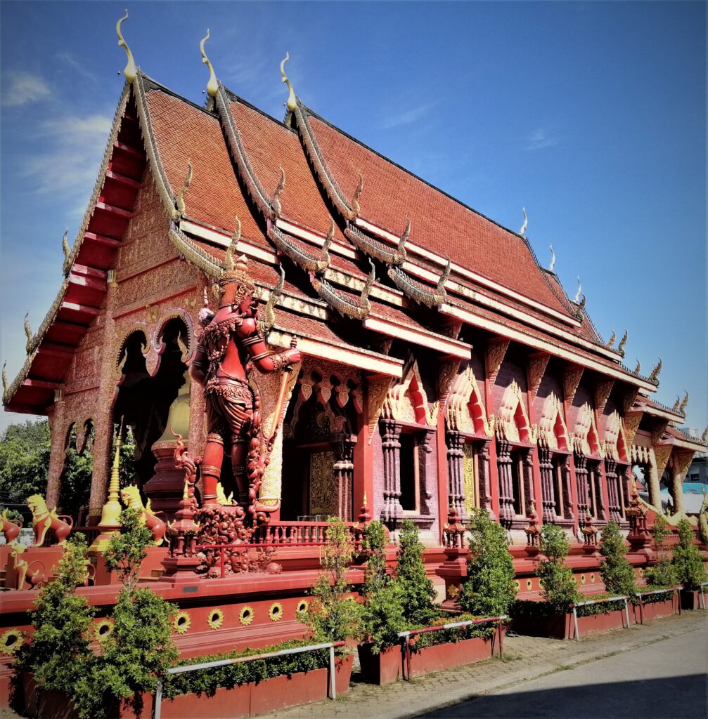 An intricately designed red temple under a mostly blue morning sky. In the post: Temple Drifting and Coffee Sipping in Chiang Rai.