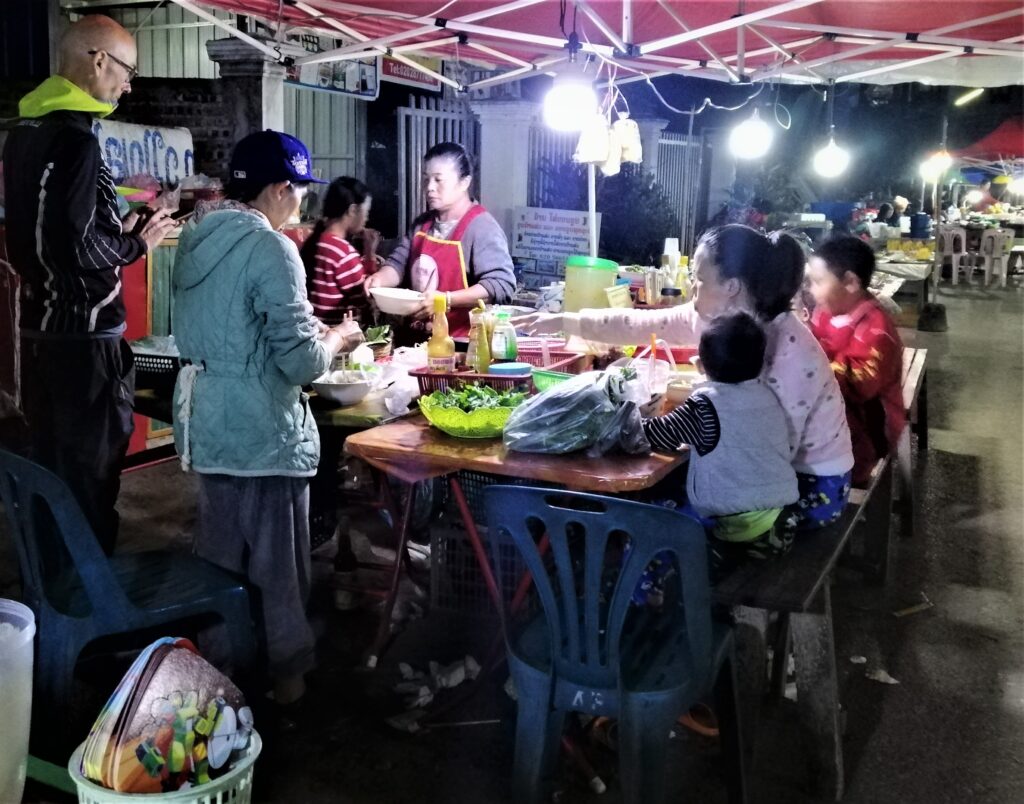 A Spanish bicycle enthusiast, Lao customers and the stall hawker at the evening food area in the center of town.  From the post: Luang Namtha: Why I Spent a Week in a Virtual Ghost Town.