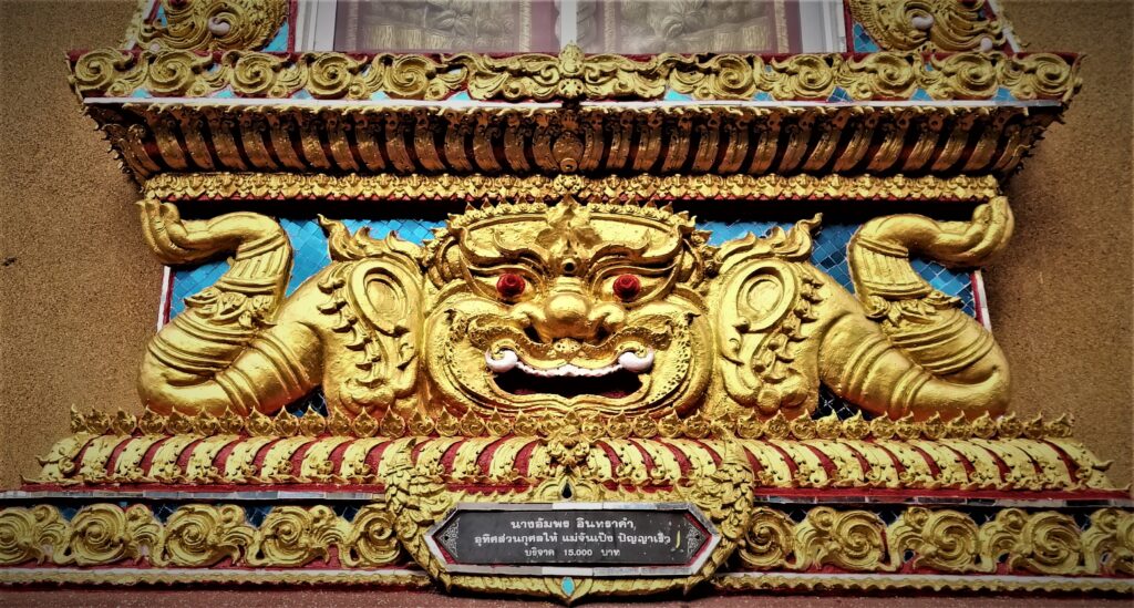 A detailed mythical being or God work of sculpture art under a temple window. In the post: Temple Drifting and Coffee Sipping in Chiang Rai.