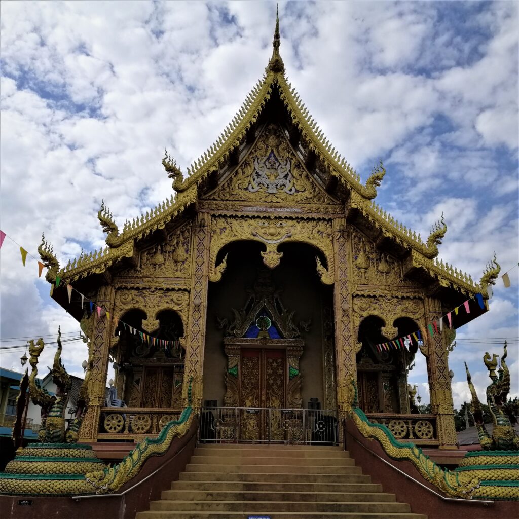 An intricately designed yellow temple under a cloudy white and blue sky.