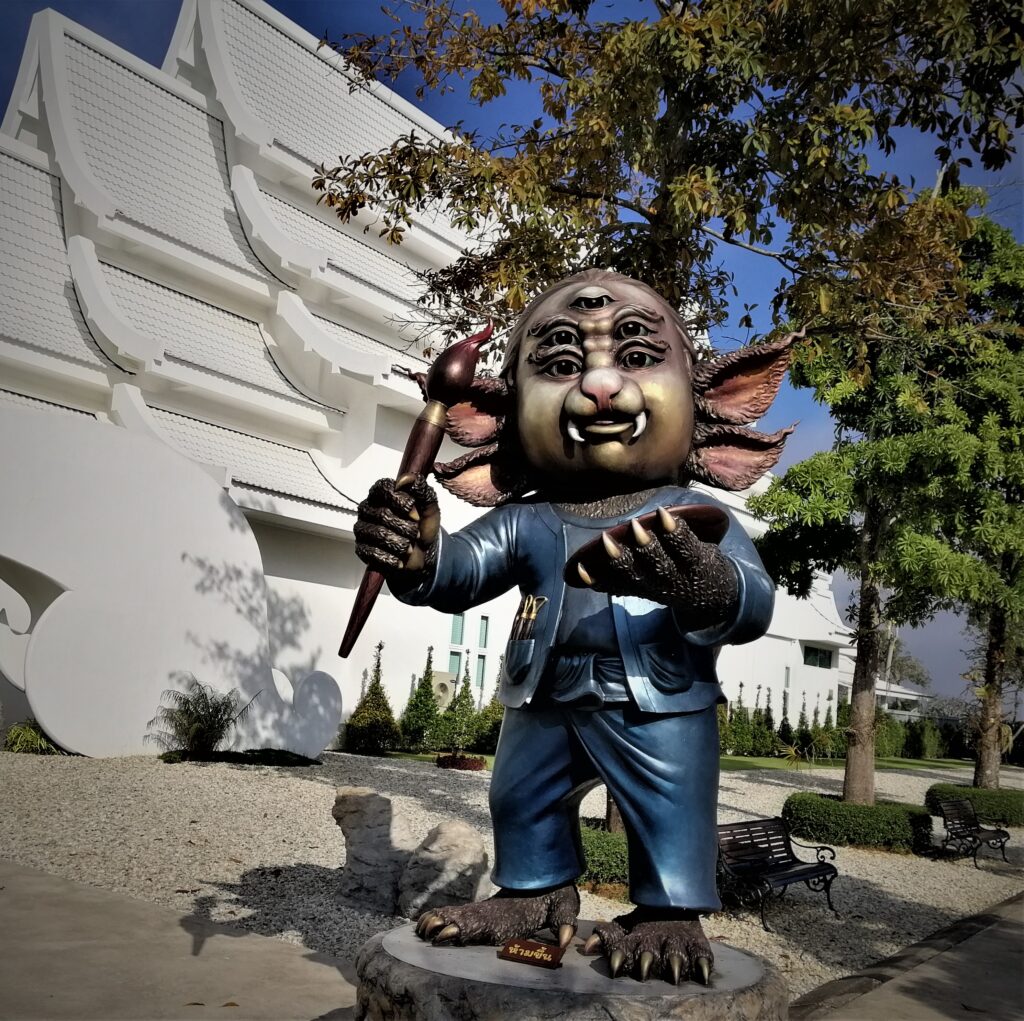 A statue of a creature with five eyes, four ears and two fags in front of a beautiful museum. In the post: Temple Drifting and Coffee Sipping in Chiang Rai.