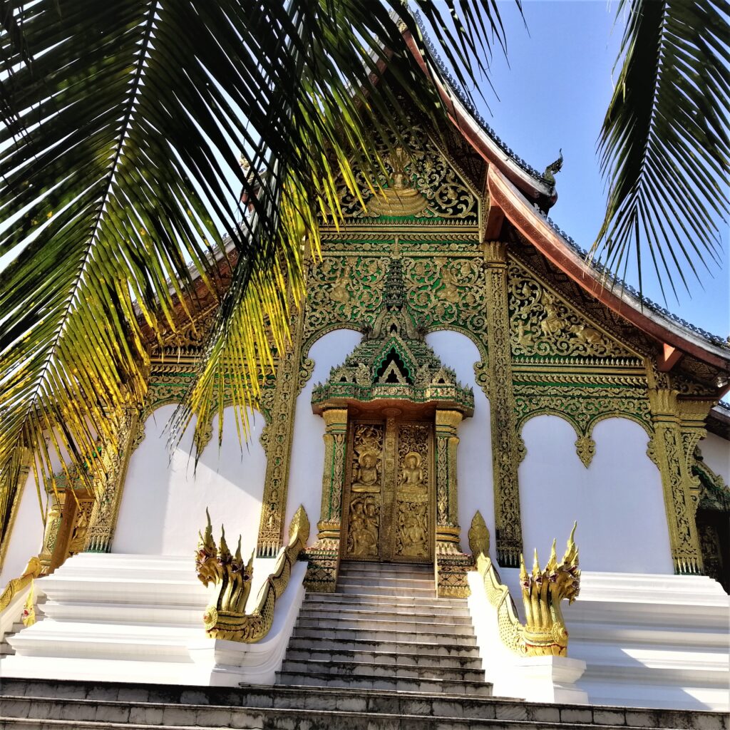 Backside of beautiful temple, an intricite door, serpants, steps, mammoth renovated wall and palm leaves. In the post: Infinite Earth Art: Temples of Luang Prabang.
