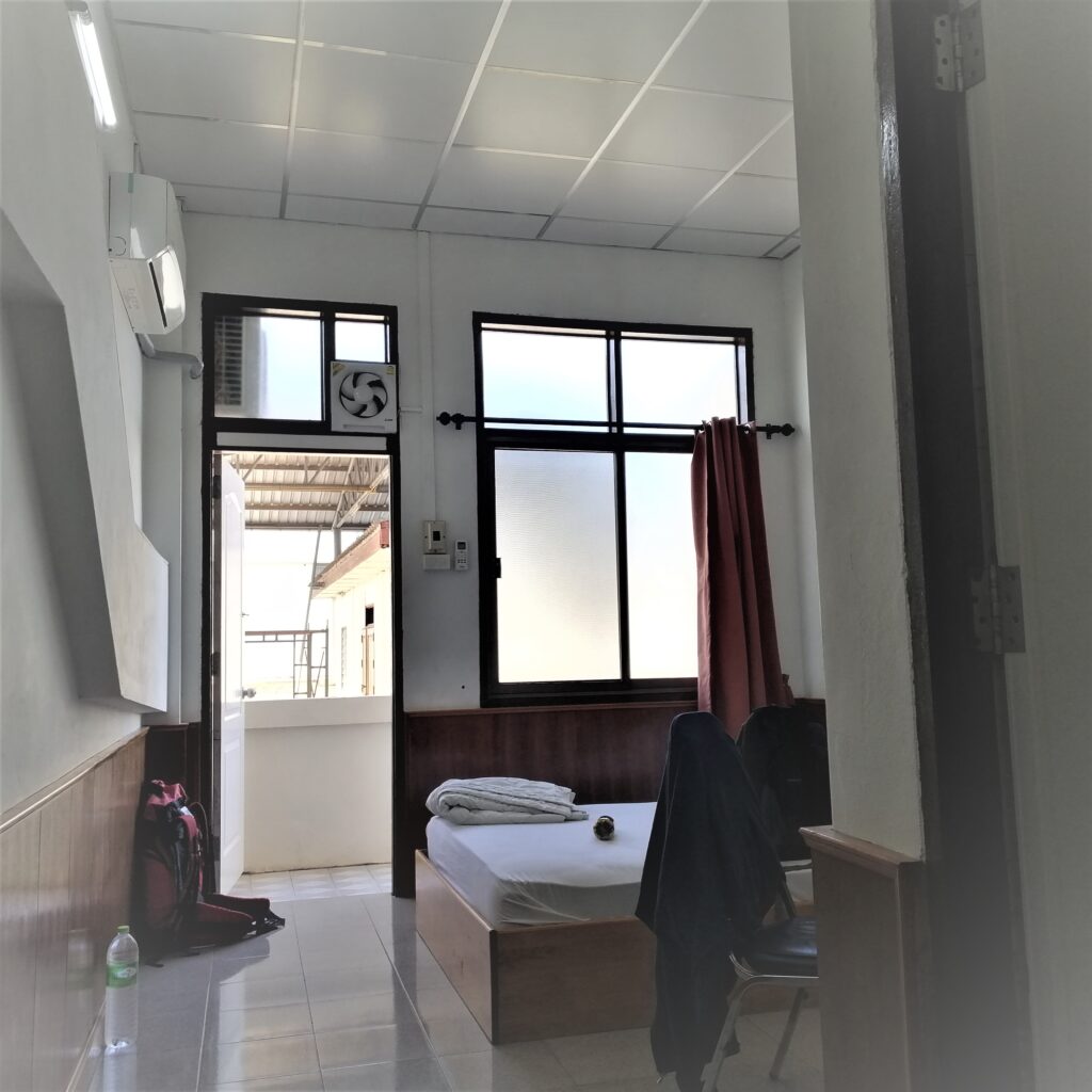 Hotel room containing chair bed, window, curtain, door to balcony, backpack and bottle of water. In article: How I traveled from Laos to Thailand for under three dollars.