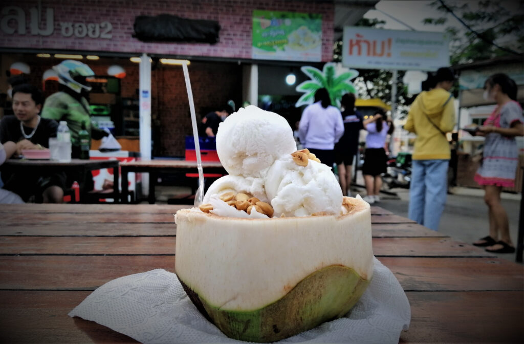 Vegan ice cream with peanuts in a coconut shell on a table.  People in the background.