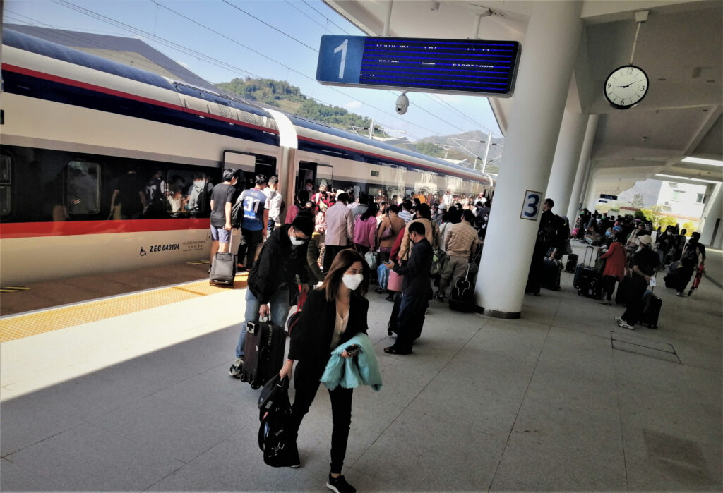 People outside in daylight leaving and getting on a high speed train on a platform at a new modern station. In post: Khon Kaen: A City of Unknown Wonders.