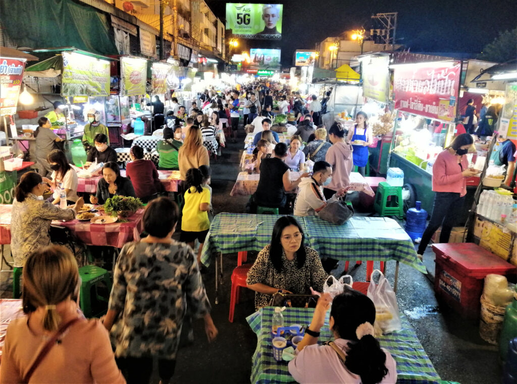 People fill tables eating, conversing and waiting alongside many food stalls. In post: Khon Kaen: A City of Unknown Wonders