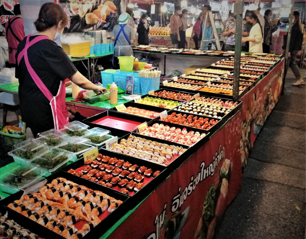 A huge sushi stall, vendor and patrons walking outside.  Thai night markets are wondrous. In post: Khon Kaen: A City of Unknown Wonders.