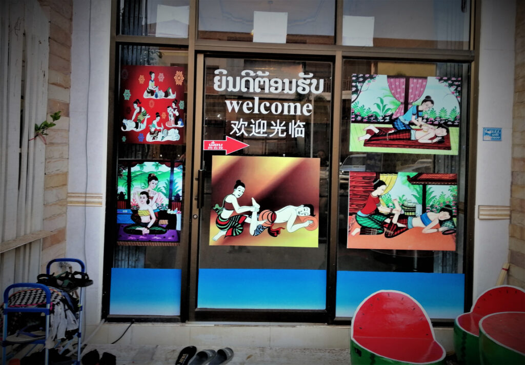 Massage parlor façade with a welcome sign and five clever and colorful paintings depicting treatment. In post: Peaceful Pakse on the Calm Mekong.