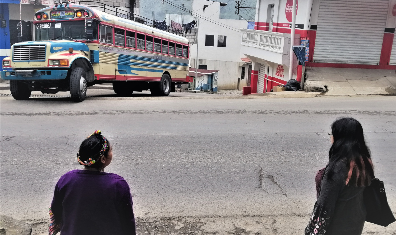 Bus coming and two Mayan women wating in Zunil in the Guatemalan highlands.