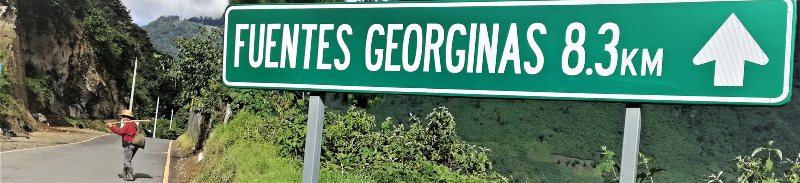 Working man walking on a road in grand nature beside a sign: 'Fuentes Georginas 8.3 km' in Zunil, Guatemala