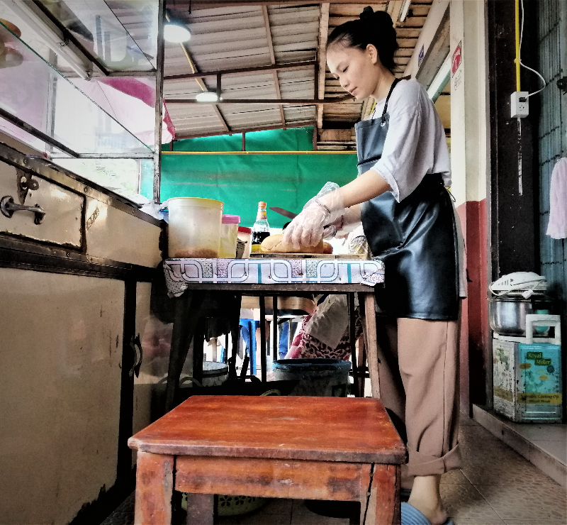 A young woman prepares a bánh mì sandwich in downtown Vientiane.