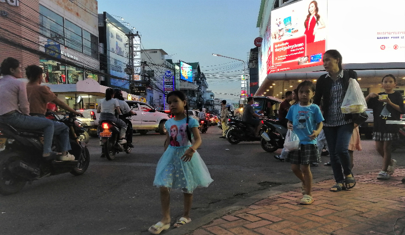 Children and other people along with multiple vehicles and shops in downtown Vientiane, Laos. 