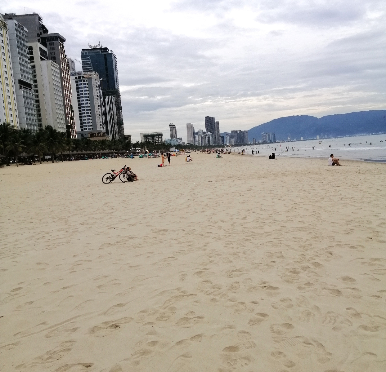Lots of luxurisouly thick sand, buildings, people, cloudy sky, sea and hills at the urban My An Beach in Danang, central Vietnam