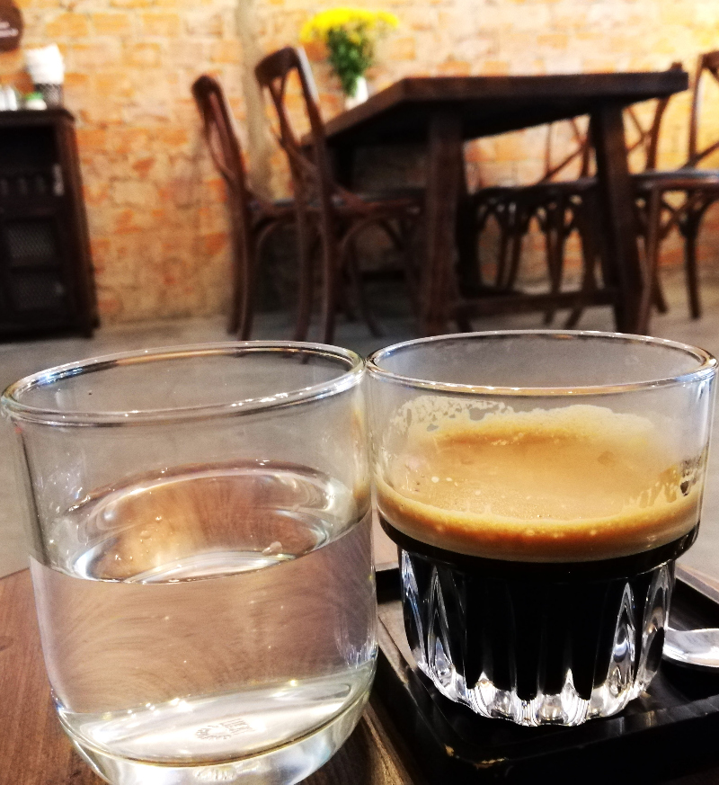 Glass of water and dark, black coffee on a tray, sitting on a stool inside Gear Café, Da Nang, Vietnam.