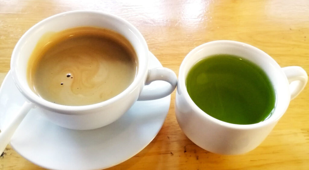 Two full hot drinks on a wooden table.  A cup of coffee and green tea, inside Fame Café, Siem Reap Cambodia.  
