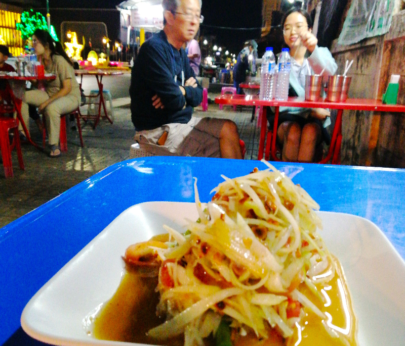 Food, papaya salad on a roadside table and customers, Nong Khai, Thailand.