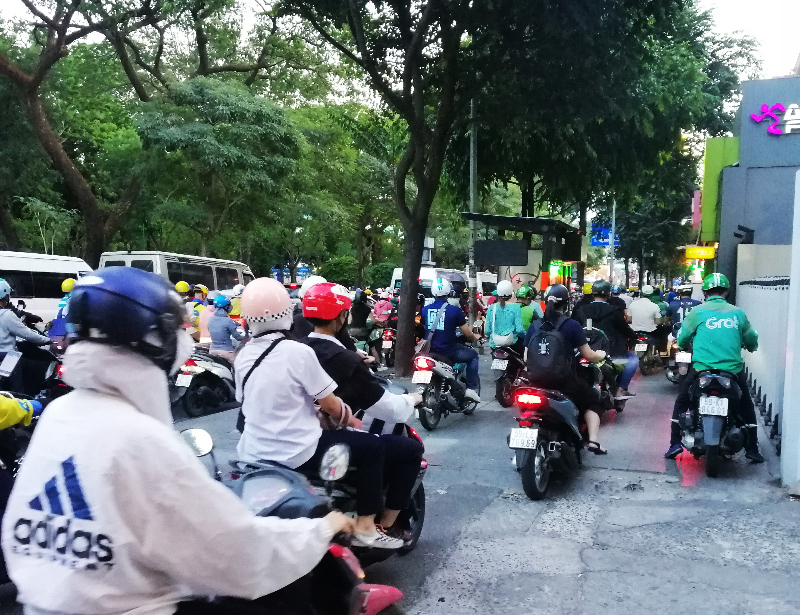 Man scooters use a wide sidewalk during morning rush hour, Ho Chi Minh City, Vietnam.